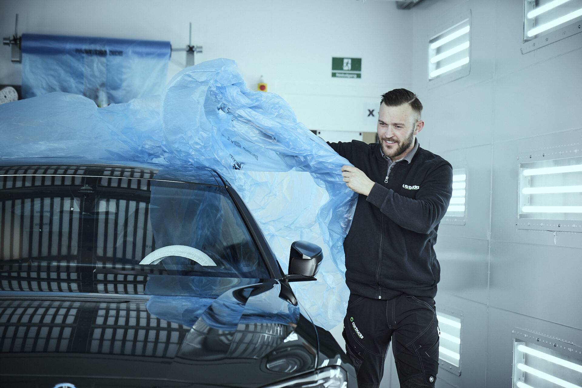 Tekniker fra Carbucks afdækker bil før lakreparation i værkstedsboks